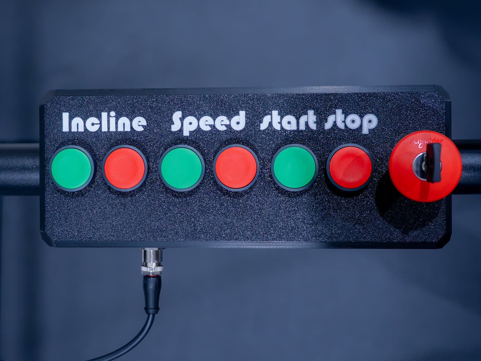 The handlebar control box in close-up: paired green and red buttons for incline, speed and start/stop, plus a key-release emergency stop.