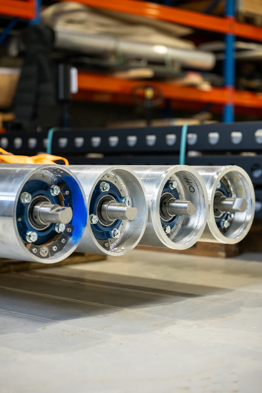 Four machined aluminium belt rollers on a pallet in the workshop.
