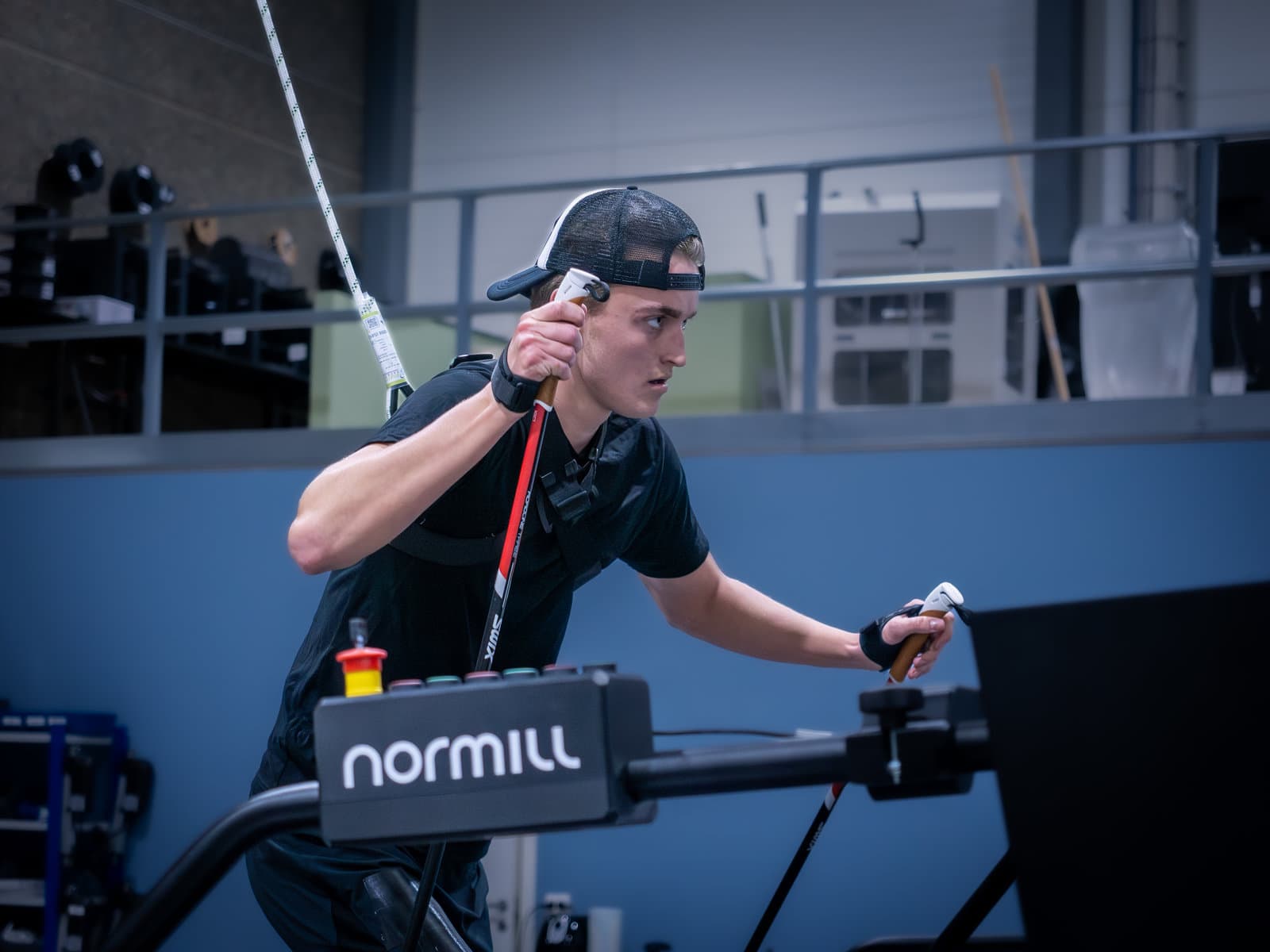 A skier in a safety harness poling on a Normill treadmill, with the control box in the foreground.