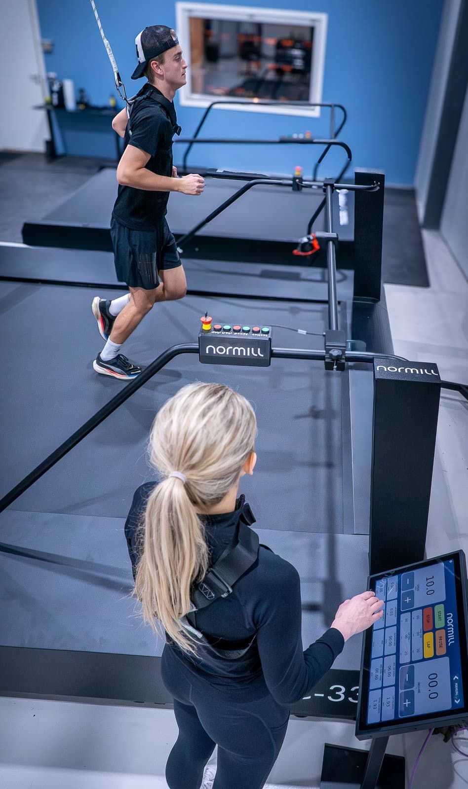 An operator adjusts the ProPanel touchscreen while an athlete trains on a Normill treadmill.
